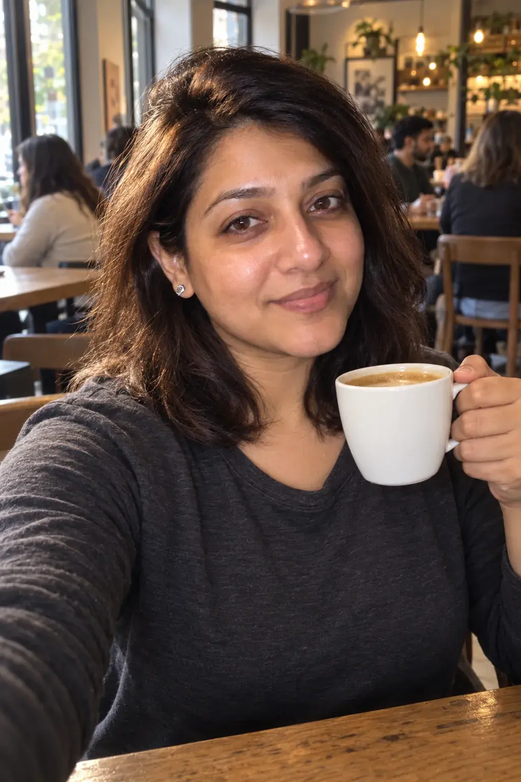 Selfie of the same woman holding a coffee in a cafe